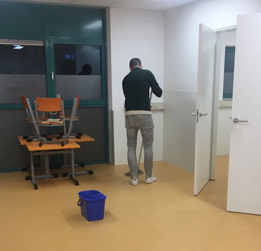 Olympus-medewerker dweilt een ruimte; stoelen staan op tafel voor de schoonmaak
