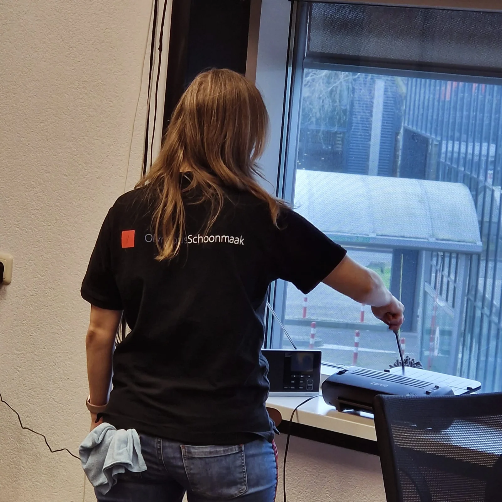 Olympus-medewerker stoft een werkplek bij het raam af; Olympus-kleding is zichtbaar
