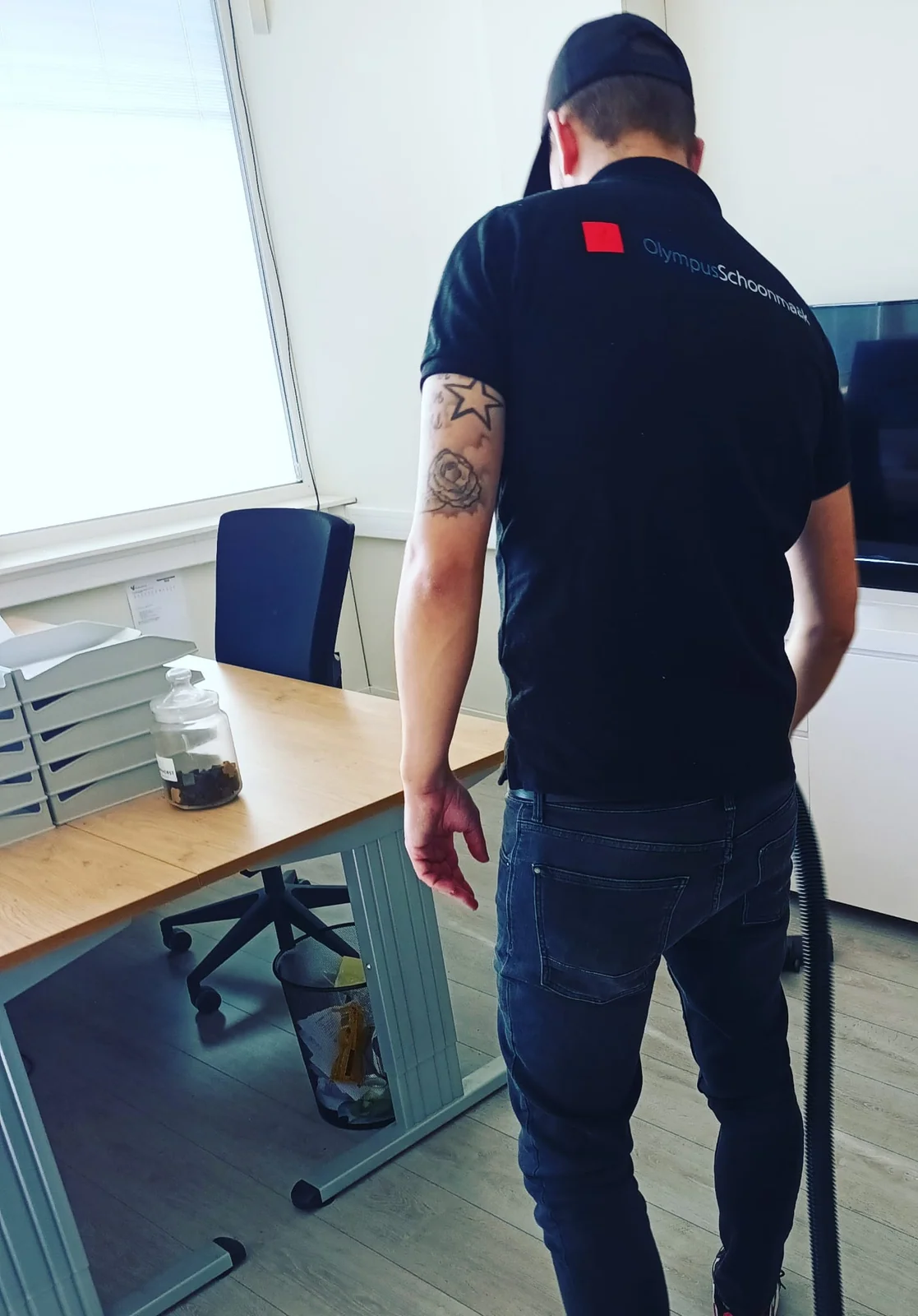 Olympus-medewerker stofzuigt tussen een bureau en een kast