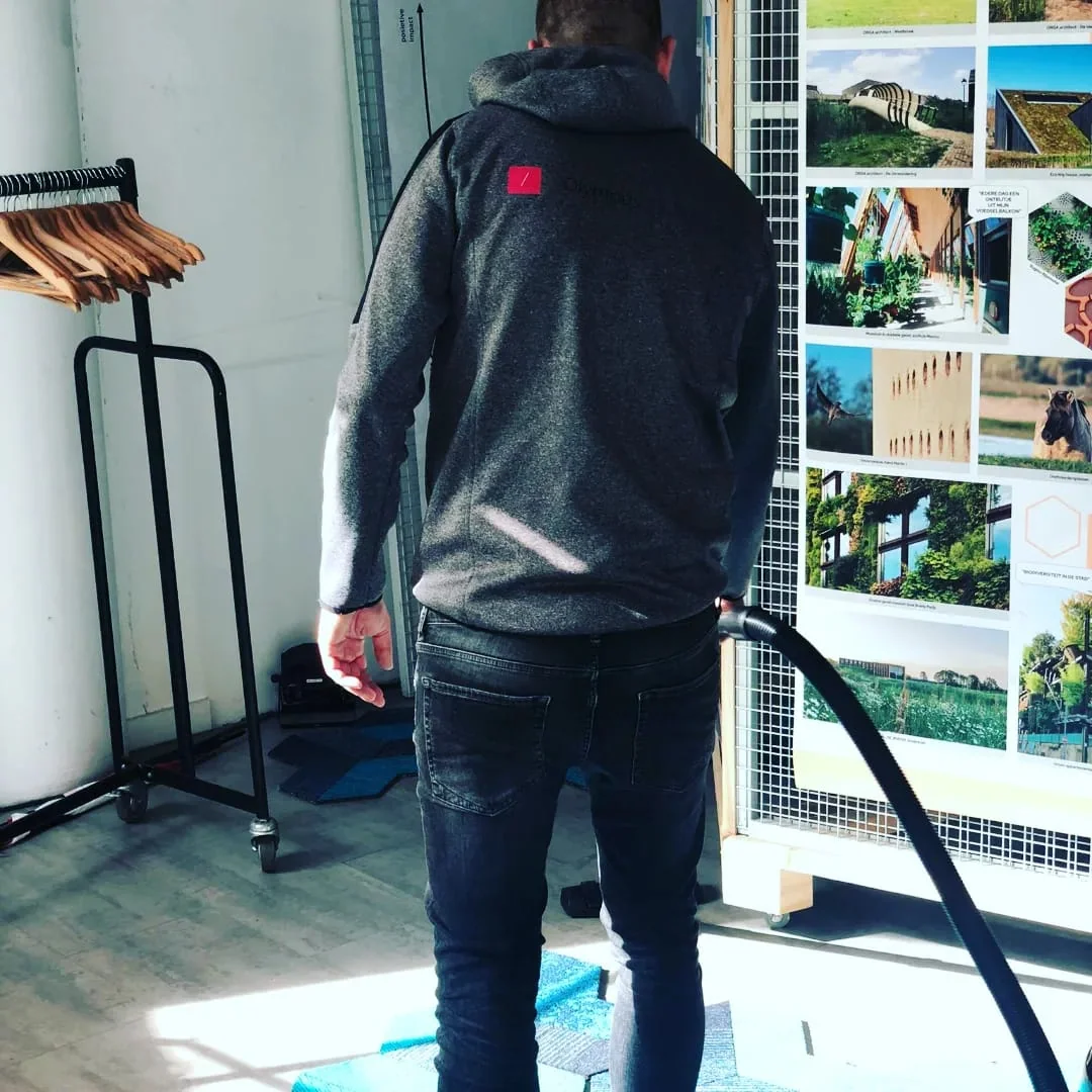 Olympus-medewerker stofzuigt een werkruimte langs een kapstok en presentatiebord
