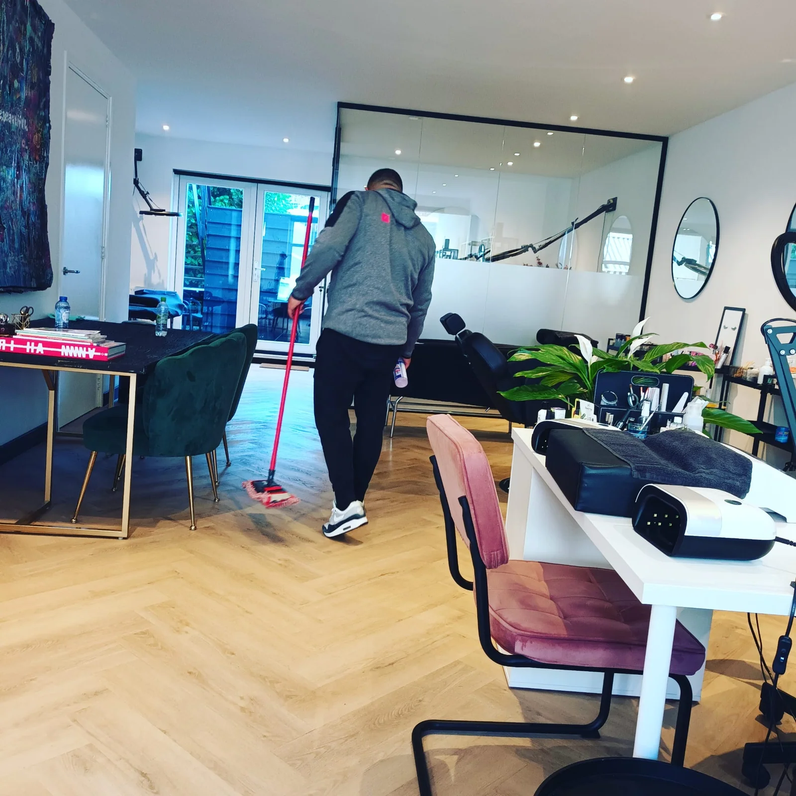 Olympus-medewerker reinigt met een vlakmop de houten vloer tussen de werkplekken van een salon